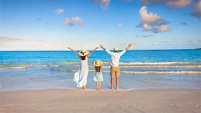 Family holding hands walking on beach with sailboat behind them